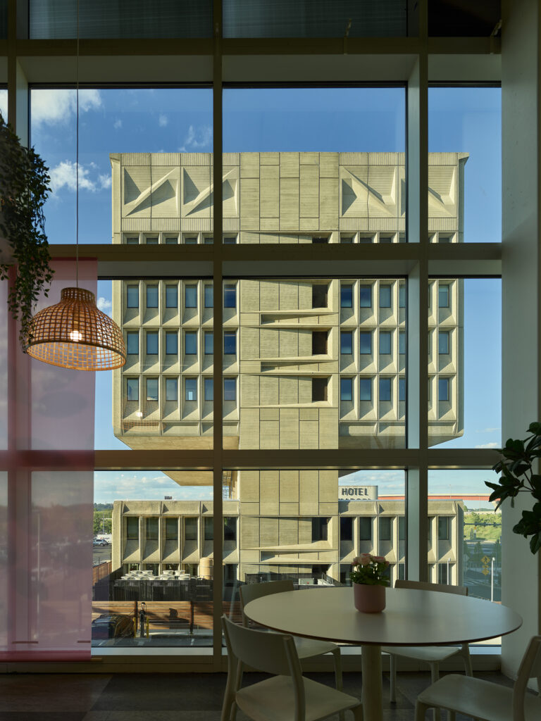 Hotel Marcel building in neutral color stone as seen through a clear window with a right hanging lamp to the side.